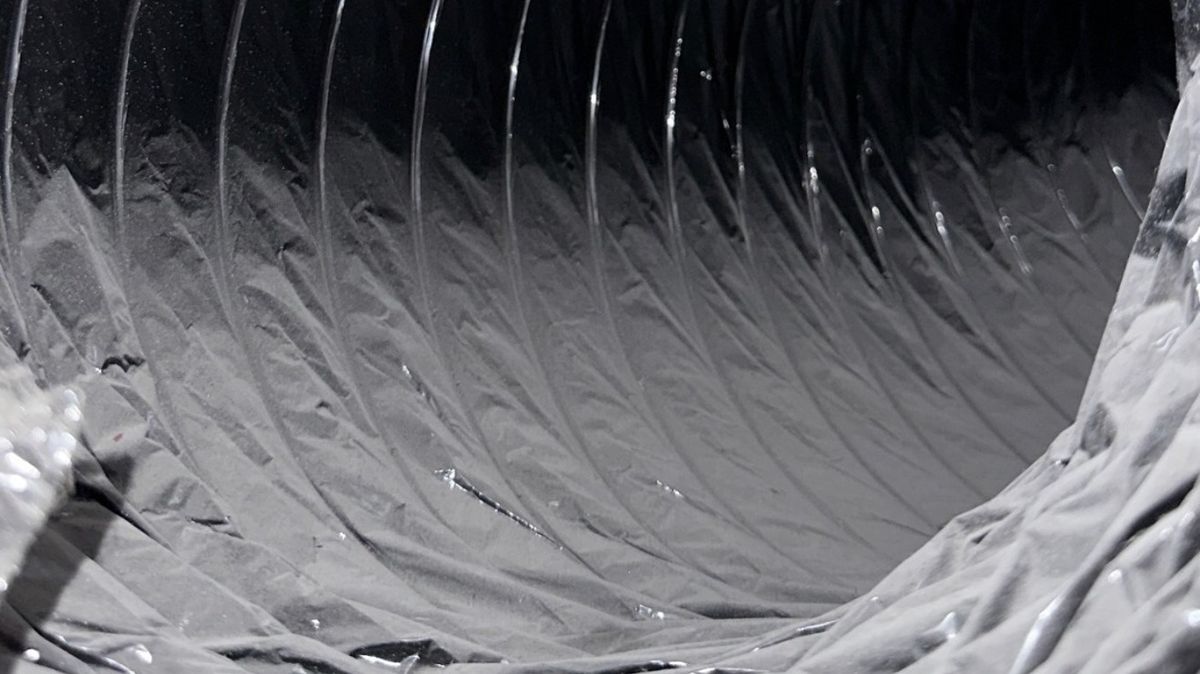 Dark flexible air duct with thick dust buildup before cleaning